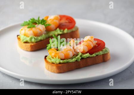 Collation saine ou bruschetta aux crevettes avec avocat et pain. Crevettes frites et purée d'avocat sur du pain grillé Banque D'Images