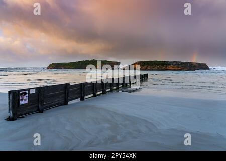 Nuages d'orage colorés et arcs-en-ciel au-dessus des îles et une groyne en bois menant dans une baie à Warrnambool sur la route Great Ocean à Victoria, en Australie. Banque D'Images