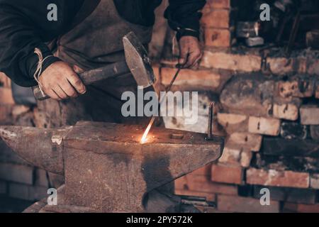 Forgeron métal brillant avec marteau sur enclume dans forge. Des mains sales de l'arrieur frappent le fer dans l'atelier. Banque D'Images