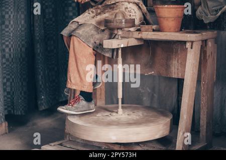 Artisan dans des vêtements de travail sales assis sur la machine de potier. Modélisation de la vaisselle sur roue dans un atelier de poterie. Banque D'Images