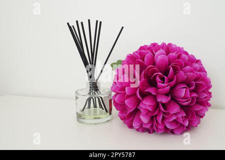 Arrangement avec des bâtonnets d'encens, huile essentielle dans un vase en verre et une fleur artificielle rose-lilas à l'intérieur d'une pièce blanche. Arrière-plan blanc Banque D'Images