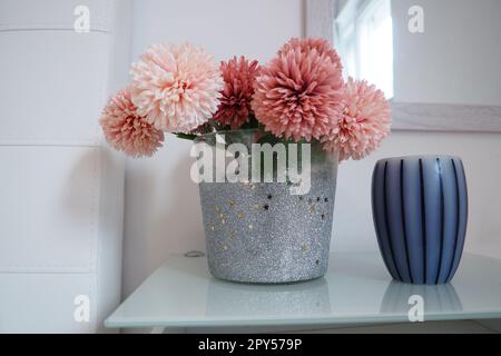 Un bouquet de belles fleurs artificielles roses sur une table blanche dans la chambre. Design intérieur. Décoration intérieure de la chambre des femmes. Bouquet dans un vase. Bougie à rayures aromatiques. Miroir sur le mur. Banque D'Images