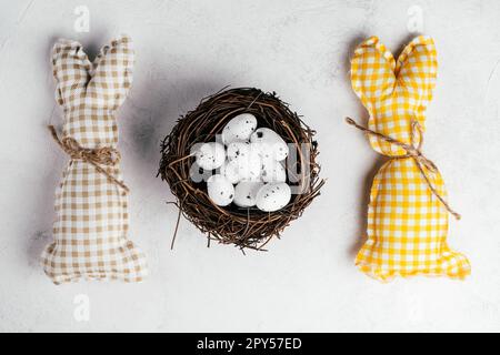 Carré de Pâques lapins faits à la main jaune et beige, œufs de caille à point blanc dans un nid brun. Fêtes traditionnelles. Banque D'Images