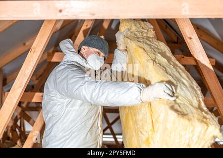 l'homme isole le toit et le plafond de la maison avec de la laine de verre Banque D'Images