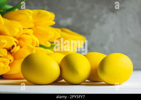 Bouquet de tulipes jaune vif et œufs de Pâques couchés sur une surface en bois blanc sur fond gris. Copier l'espace Banque D'Images