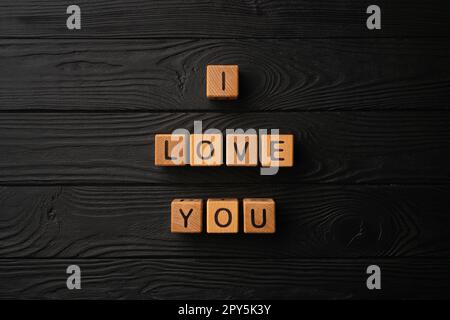 Cubes en bois avec l'expression Je vous aime sur fond noir - une table en bois. Les mots d'amour sont faits de lettres de bois pour votre petite amie, petit ami, femme, mari, pour la Saint-Valentin salutation carte postale romantique. Banque D'Images