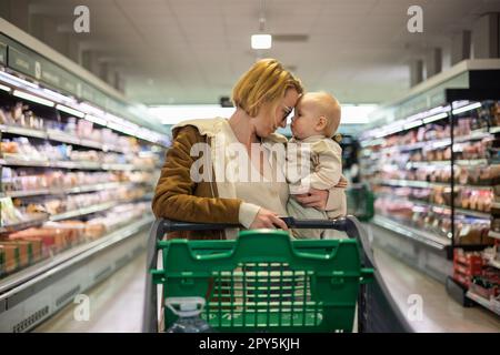 Mère poussant le chariot avec son bébé garçon enfant dans l'allée du rayon dans l'épicerie du supermarché. Concept shopping avec enfants. Banque D'Images