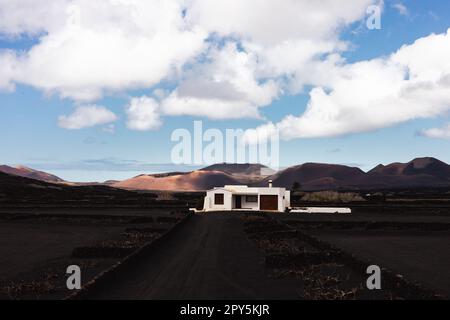 Maison blanche traditionnelle dans le paysage volcanique noir de la région viticole de la Geria avec vue sur le parc national de Timanfaya à Lanzarote. Attraction touristique sur l'île de Lanzarote, îles Canaries, Espagne. Banque D'Images