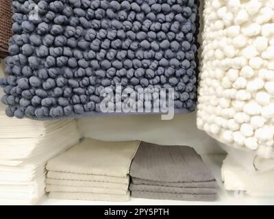 Les tapis de bain en microfibre blanc et gris sont suspendus au comptoir du magasin. Style scandinave. Tapis rectangulaires en tissu doux avec boutons tricotés. Décoration et design moderne de la salle de bains Banque D'Images