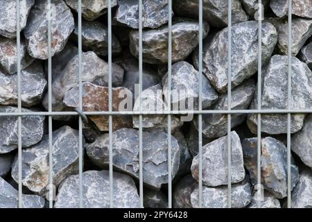 Les pierres brutes bordent et le mur de pierres grises comme fond de pierres naturelles avec des matériaux broyés et rugueux empilés dans la grille métallique comme bordure massive dans les couleurs grises comme fond minéral naturel pour les jardins Banque D'Images