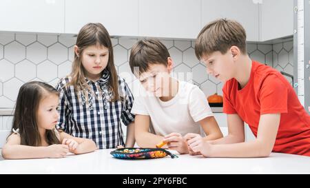 Un groupe d'amis jouent à la pêche sur une table de cuisine. Smart boy tient la canne à pêche et ramasser les articles de jeu de l'assiette. Banque D'Images