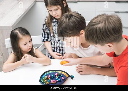 Un groupe d'amis joue à la pêche en jouet sur une table. Les enfants tiennent la canne à pêche et ramassent des articles de jeu en métal coloré de l'assiette. Banque D'Images