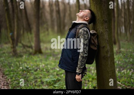 Portrait de l'homme avec sac à dos pendu son dos contre un arbre sur la forêt. Amour de la nature. Banque D'Images