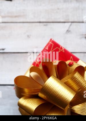 Boîte cadeau rouge avec un grand noeud doré sur un fond en bois peint avec de la peinture blanche. Cadeau de Noël, nouvel an, anniversaire, Fête des mères, mariage, Saint Valentin. Belle décoration de fête Banque D'Images