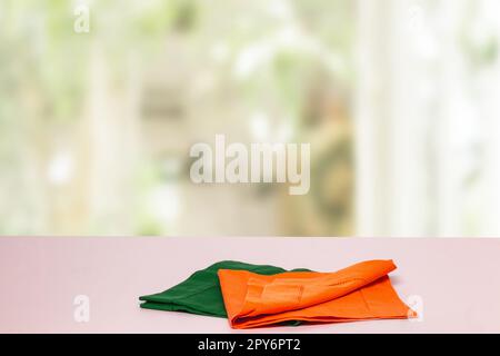 Produit de table vide. Gros plan d'une nappe ou d'une serviette orange et verte vide sur une table lumineuse sur un arrière-plan de rideaux flous. Modèle pour le montage des produits alimentaires et de présentation. Banque D'Images