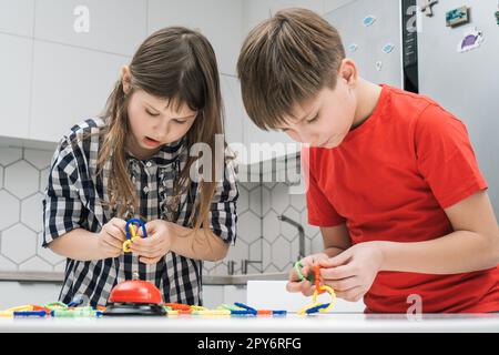 Les enfants jouent jouet constructeur debout au-dessus de la table de cuisine et regardant vers le bas. Garçon et fille collectent les détails en plastique de lego. Banque D'Images