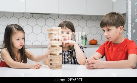 Les enfants de l'école concentrée jouent tour assis à table de cuisine. Garçons et filles construisent tour à partir de petits blocs de bois. Banque D'Images