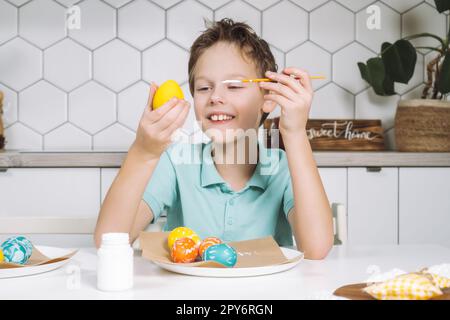 Portrait sourire joyeux petit garçon, peinture multi coloriage poules de Pâques oeufs table en papier avec pinceaux. Gros plan Banque D'Images