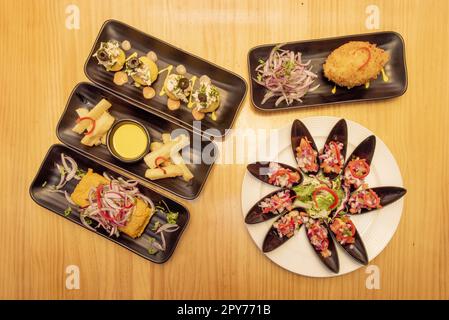 Ensemble de plats péruviens colorés avec moules fraîches, anticuchos grillés, riz blanc, lomo saltado, causa lima, yucca frit sur une table en pin Banque D'Images