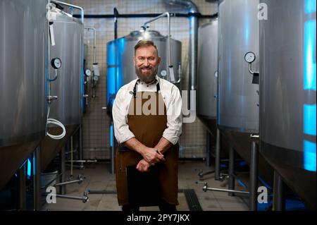 Portrait d'un brasseur souriant en tablier debout parmi les cuves de la distillerie Banque D'Images