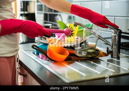 Évier de cuisine plein de vaisselle sale. Femme en gants de caoutchouc rose faisant la vaisselle, en utilisant la brosse. Comptoir de couleur sombre dans la cuisine moderne. Corvées de maison Banque D'Images