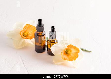 Sérum visage dans des flacons cosmétiques en verre avec pipette pour les soins quotidiens de la peau sur fond blanc texturé avec des jonquilles frais. cosmétiques naturels Banque D'Images