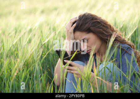 Triste femme lisant le chat téléphonique dans un champ Banque D'Images