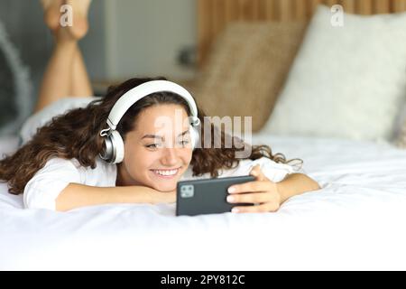 Bonne femme regardant des vidéos sur un smartphone sur un lit Banque D'Images