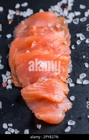 Filets de saumon frais crus. Carpaccio de saumon servi avec du sel sur une planche à découper noire Banque D'Images