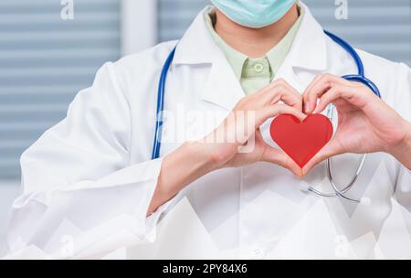 Gros plan du médecin femme portant un manteau blanc debout faisant le coeur de la forme du doigt Banque D'Images