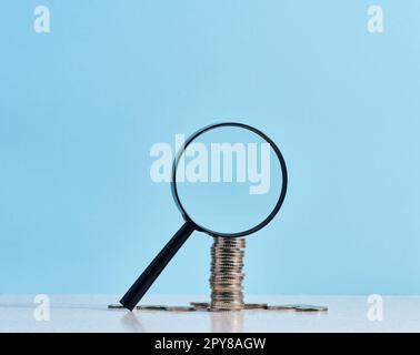 Une pile de pièces de monnaie en métal et une loupe en plastique sur fond bleu. Le concept de l'augmentation des impôts, des subventions Banque D'Images