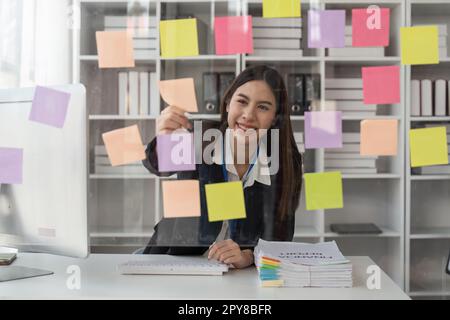 Des idées de planification de femme d'affaires heureuse sur un mur de verre avec des notes adhésives colorées à l'intérieur d'un bureau Banque D'Images