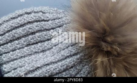 Bonnet tricoté avec un gros plan de citrouille sur un fond principal gris. Publicité pour vêtements d'hiver. Saison d'hiver. Couleurs grises et brunes. Grosses boucles. Le pumpon brun de fourrure naturelle. Banque D'Images