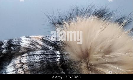 Bonnet tricoté avec un gros plan de citrouille sur un fond principal gris. Publicité pour vêtements d'hiver. Saison d'hiver. Tons gris blanc, beige, marron et noir. Grosses boucles. Le pumpon brun haricot de fourrure naturelle Banque D'Images