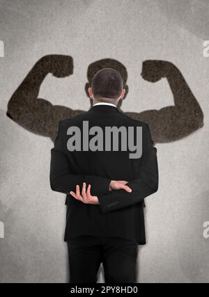 Homme d'affaires et ombre d'un homme musclé fort devant lui sur le mur gris. Concept de résistance intérieure Banque D'Images