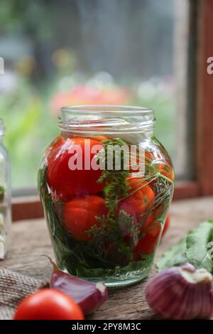 Pot en verre avec légumes, herbes et saumure sur une table en bois à l'intérieur Banque D'Images