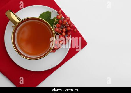 Tasse de thé et baies de viburnum mûres fraîches sur table blanche, vue du dessus. Espace pour le texte Banque D'Images