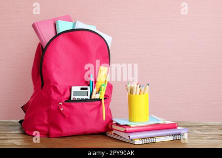 Sac à dos avec papeterie scolaire sur table en bois sur fond rose Banque D'Images