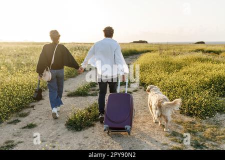 Un jeune couple épris inspiré regarde le plan de vie à l'avenir. Ils sont debout avec une valise et ukulele, tenant les mains. Recherche d'une nouvelle homela Banque D'Images