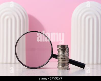 Une pile de pièces de monnaie en métal et une loupe en plastique sur fond rose. Le concept de l'augmentation des impôts, des subventions Banque D'Images