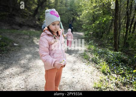 Petite fille avec fleurs périwinkle dans la forêt de printemps. Banque D'Images
