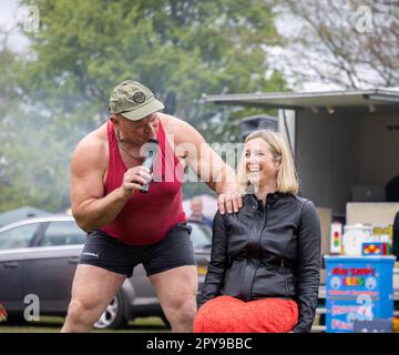 Culcheth, Royaume-Uni. Lundi 1 mai 2023, Culcheth, Angleterre - malgré les cieux gris et la bruine, Culcheth et Glazebury Community Day sur le green du village, qui propose des divertissements par Ian “Zippy” Lees, Northern Stars Dance & Fitness et le Mighty Smith strongman Show, avec des sidestals et des foires funestes. Adrian Smith parle à une femme assise sur une chaise avant qu'il la lève dans l'air crédit: John Hopkins/Alamy Live News Banque D'Images