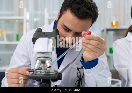 Scientifique mâle laissant tomber du liquide chimique sur lame au microscope. Science et technologie concept. Banque D'Images