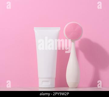 Tube en plastique blanc et brosse de massage pour le nettoyage du visage sur fond rose, articles pour les procédures cosmétiques Banque D'Images