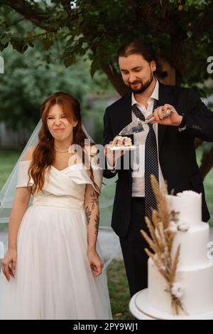 les jeunes mariés coupent joyeusement et goûtent le gâteau de mariage Banque D'Images