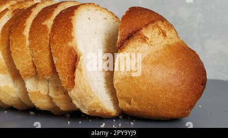 Pain tranché de farine de blé. Tranches appétissantes de pain blanc avec croûte croustillante cuite. Produit contenant du gluten. Pain frais. Fond gris. Miettes sur la table. Banque D'Images