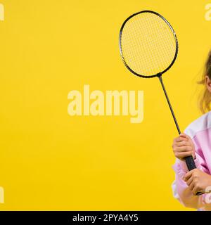 Photo studio pleine longueur d'une fille de dix ans tenant une raquette de badminton et isolée sur le jaune. Banque D'Images