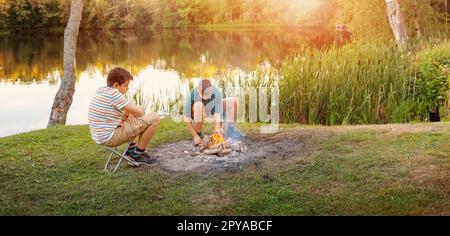 Deux adolescents éclairant un feu de camp dans la nature près du lac. Banque D'Images