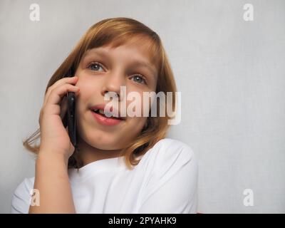 fille de 7 ans sans dent de devant. L'enfant sourit, regarde loin et parle au téléphone ou au smartphone. Changement des dents de lait chez l'enfant. Orthodontie et pratique dentaire Banque D'Images