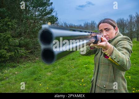 Une femme de plus de trente ans avec un fusil de chasse en gros regardant le canon Banque D'Images